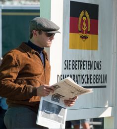 a man reading a newspaper in front of a sign