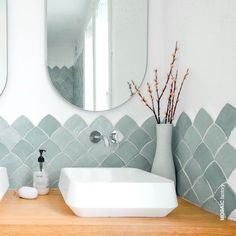 a white sink sitting under a bathroom mirror next to a vase with flowers in it