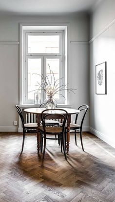 a dining room table with four chairs and a vase on top of it in front of a window