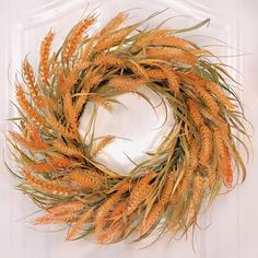 an orange wreath is hanging on a white door with some grass in the middle and one piece of paper behind it