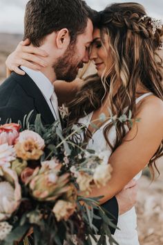 a bride and groom embracing each other in front of the desert with their wedding bouquet