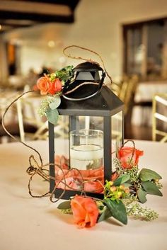 a lantern with flowers and greenery on top of a white table cloth covered table