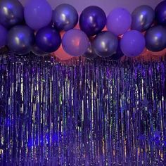 balloons and streamers are hanging from the ceiling in front of a purple wall with sequins