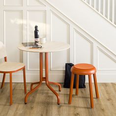 two chairs and a table in front of a white wall with wood flooring on it