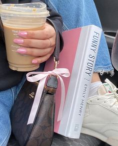 a person holding a book and a drink in their hand while sitting on the back seat of a car