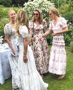 three women in dresses talking to each other at a picnic table with flowers on it