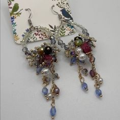 a pair of earrings with beads and chains on top of a white table next to a card