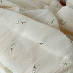 an unmade bed with white linens and green embroidered flowers on the sheet cover