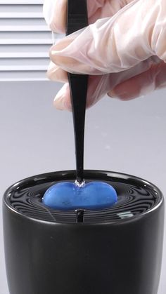 a person in white gloves is pouring liquid into a black container with a blue substance on it