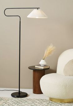 a floor lamp next to a white chair and table with a book on it in a living room