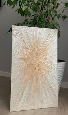 a white vase sitting next to a plant on top of a wooden floor