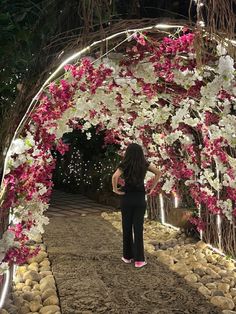 a woman standing in front of a flower covered archway with lights on each side and flowers all around the arch