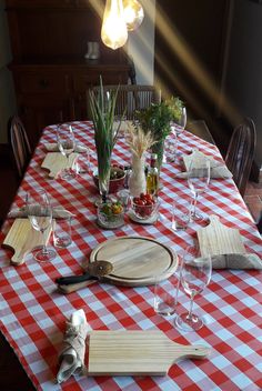 a table set with plates, utensils and wine glasses on top of a checkered table cloth