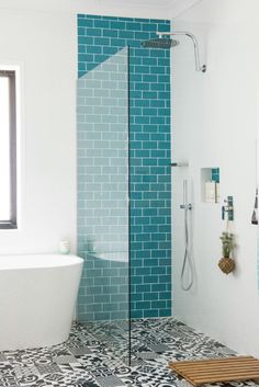 a white bath tub sitting next to a walk in shower under a window with blue tiles on the walls