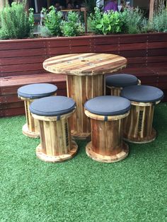 four stools and table made out of wood on the grass in front of a wooden bench