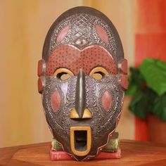 a decorative mask on a wooden table in front of a potted plant and window