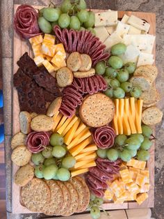 an assortment of cheeses, crackers, and grapes on a wooden platter