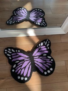 two butterfly shaped rugs sitting on the floor in front of a mirror, one with purple and white wings