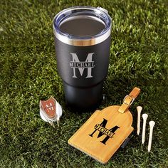 a travel mug and luggage tags are on the grass next to a pair of golf tees