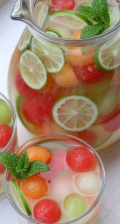 a jar filled with watermelon, lemon and grapefruit next to two glasses