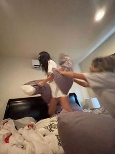 two girls jumping on a bed in a room with white walls and carpeted floors