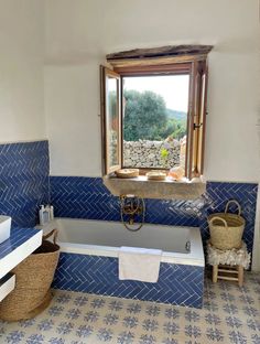 a bathroom with blue and white tile on the floor, tub, sink and window