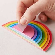 a hand holding a piece of paper over a rainbow coaster