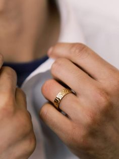 a man wearing a gold wedding band and a ring on his left hand is adjusting the collar of his white shirt