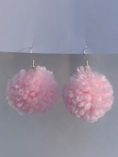 two pink pom - poms hanging from hooks on a gray surface with a white wall in the background