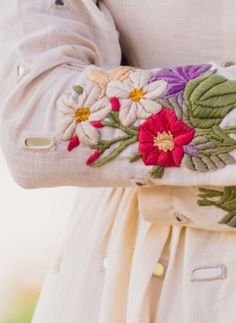 a woman wearing a white dress with colorful flowers on it's sleeves and belt