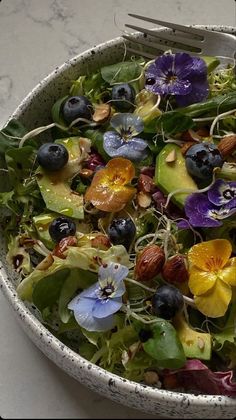 a salad with blueberries, avocado, and other flowers in a bowl