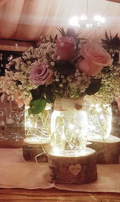 some flowers are sitting in glass jars on a table with candles and lights around them