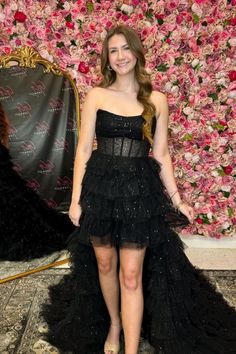 a woman standing in front of a floral wall wearing a black dress and high heels