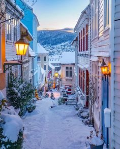 an alley way with snow on the ground and street lights in front of buildings at dusk