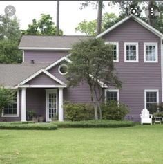 a purple house with two white chairs in the front yard and trees on either side