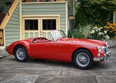 an old fashioned red sports car parked in front of a house with stairs leading up to it