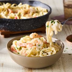 a spoon full of pasta with shrimp and parmesan cheese in it, being lifted from a bowl