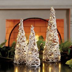 three white christmas trees sitting on top of a table next to a fireplace in a living room