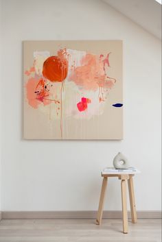 an abstract painting hangs on the wall next to a stool