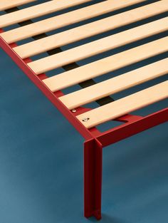 a wooden bed frame with red slats and black dots on the bottom part, against a blue background