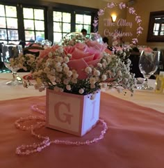 pink roses and white flowers in a square vase on a table with a name plate