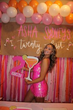 a woman in a pink dress standing next to a table with balloons and drinks on it