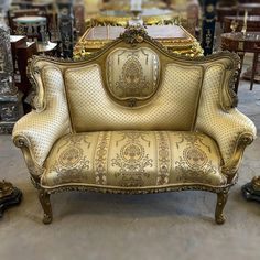 an ornate gold couch sitting on top of a floor next to other antique chairs and tables