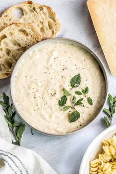 two bowls filled with soup next to slices of bread and sprigs of parmesan cheese