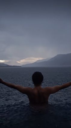 a man standing in the water with his arms spread out and hands outstretched to the sky