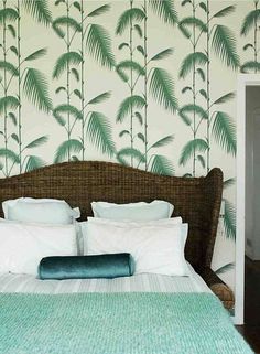 a bed with white pillows and green palm leaves on the wall next to a door