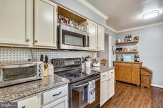 a kitchen with white cabinets and stainless steel stove top oven next to wooden flooring