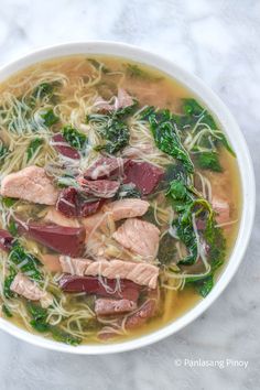 a bowl of soup with meat, noodles and spinach on a marble countertop