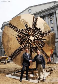 two men shaking hands in front of a large metal object that looks like a snowflake