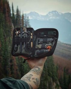 a person holding an open case with tools in it on top of a mountain range